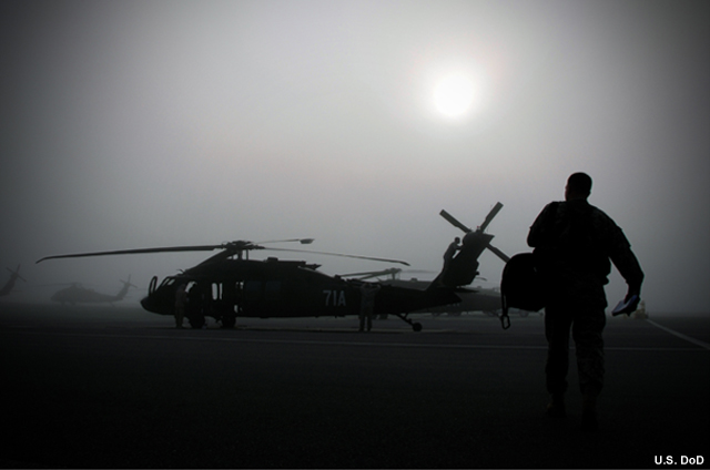 Photograph of a man walking to a one of several helicopters in the fog