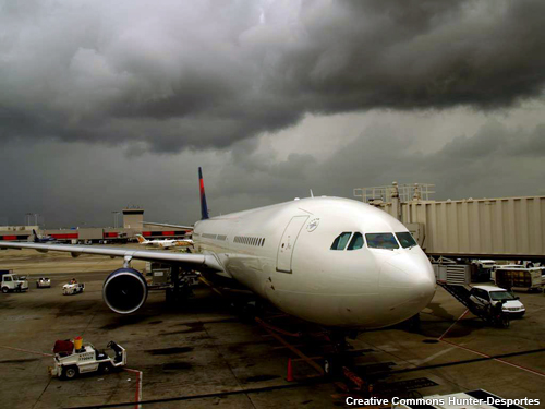 A commercial airliner is parked at a terminal with heavy dark gray clouds hanging over the airport.