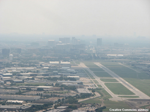 Thick haze obscures the city skyline next to the airport as an airplane approaches to land.