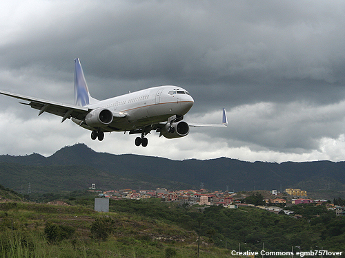 A passenger jet is preparing to land on an airport located in a mountainous region.  Low, grey clouds obscure the sky.