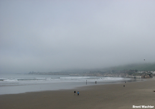 Low clouds move inwards from the ocean over the California coast.  The clouds have come over the beach and reached the nearby mountains.